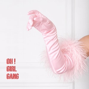 May include: A pair of light pink satin gloves with a fluffy feather trim at the wrist. The text "OH! GIRL GANG" is displayed in red on the left side of the image. The gloves are elegant and stylish.