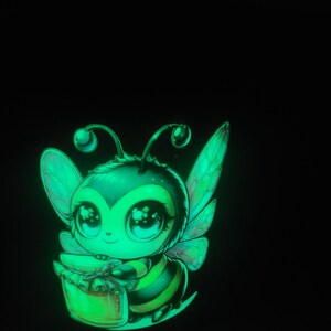 Może przedstawiać: Świecący kreskówkowy pszczoła z dużymi oczami, skrzydłami i czułkami, trzymający słoik miodu. Pszczoła jest zielona, czarna i żółta, z uroczym, przyjaznym wyrazem twarzy. Obraz jest na czarnym tle.