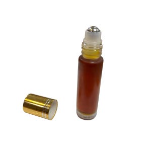 Könnte beinhalten: Eine transparente Glas-Rollflasche mit goldfarbenem Verschluss und einer silbernen Rollkugel. Die Flasche ist mit einer braunen Flüssigkeit gefüllt.