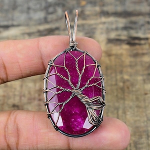 Peut inclure: Un pendentif en forme d'arbre de vie en pierre rose avec un enroulement de fil de cuivre. Le pendentif est de forme ovale et présente un design d'arbre détaillé.