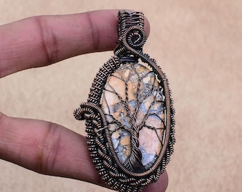 May include: Oval pendant with a stone featuring a tree design, encased in copper wire. The stone has a beige and gray pattern. The wirework is intricately woven around the stone, creating a unique, handcrafted piece of jewelry.