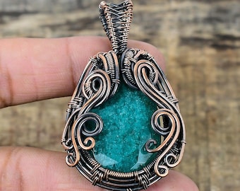 May include: A teal green gemstone pendant wrapped in copper and silver wire. The wire is twisted and curled into a decorative design.