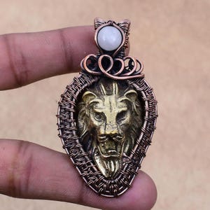 May include: A copper wire wrapped pendant featuring a lion head design with a white stone at the top.