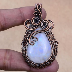 May include: A teardrop-shaped moonstone pendant with a copper wire wrap. The wire wrap features intricate swirls and a bail for hanging.
