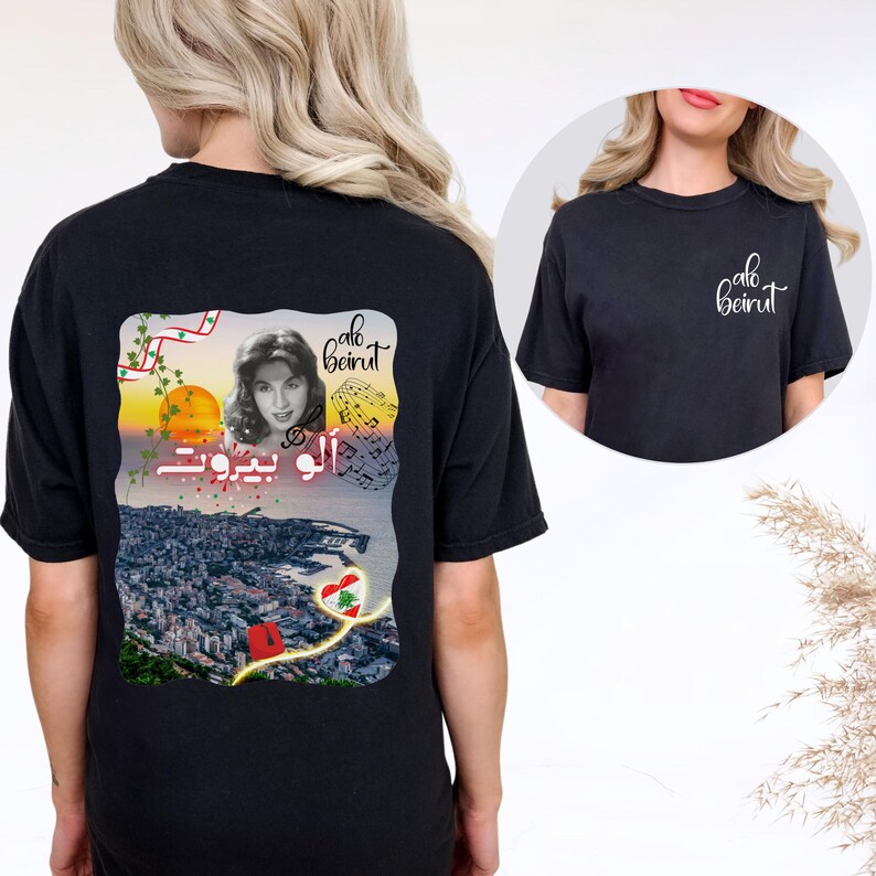 Puede incluir: Una camiseta negra con un gr&aacute;fico en la espalda y un logotipo peque&ntilde;o en la parte delantera. El gr&aacute;fico trasero muestra un retrato de Fairuz, el texto "alo beirut" en ingl&eacute;s y &aacute;rabe, notas musicales, un atardecer y un coraz&oacute;n con la bandera.