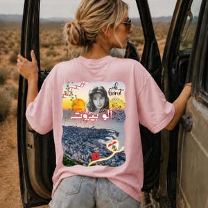 Puede incluir: Una camiseta rosa claro con un gr&aacute;fico en la espalda que muestra el retrato de una mujer, el texto "alo beirut" en ingl&eacute;s y &aacute;rabe, notas musicales, un atardecer sobre una ciudad costera, un coraz&oacute;n con la bandera libanesa y enredaderas.