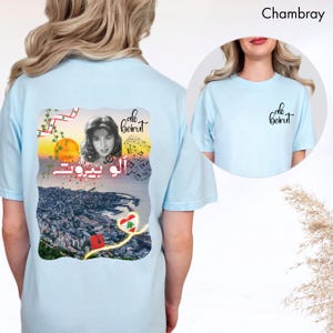 Puede incluir: Una camiseta azul claro con un gr&aacute;fico en la espalda que muestra un retrato en blanco y negro de una mujer, notas musicales, un atardecer sobre una ciudad, un fez rojo y un coraz&oacute;n con la bandera libanesa. El texto dice Alo Beirut.