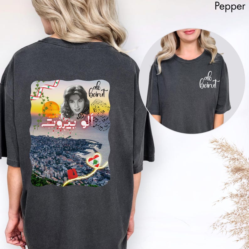 Puede incluir: Una camiseta gris carb&oacute;n con un gr&aacute;fico en la espalda y un logotipo peque&ntilde;o en el frente. El gr&aacute;fico trasero muestra el retrato de una mujer, un atardecer sobre una ciudad, notas musicales, el texto "alo beirut" en ingl&eacute;s y &aacute;rabe, y un coraz&oacute;n con la bandera libanesa.