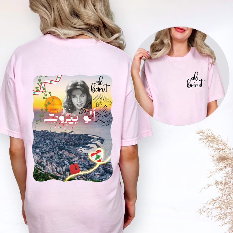 Puede incluir: Una camiseta rosa claro con un gr&aacute;fico en la parte posterior y un logotipo m&aacute;s peque&ntilde;o en el frente. El gr&aacute;fico posterior muestra el retrato de una mujer, notas musicales, un atardecer sobre una ciudad costera y el texto "alo beirut" en ingl&eacute;s y &aacute;rabe.