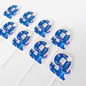 Puede incluir: Un conjunto de nueve adornos para tartas con el n&uacute;mero nueve y el personaje Stitch de Lilo & Stitch. Cada adorno tiene un n&uacute;mero nueve azul con una ilustraci&oacute;n de Stitch y un palito blanco. El fondo del n&uacute;mero nueve es un patr&oacute;n azul.