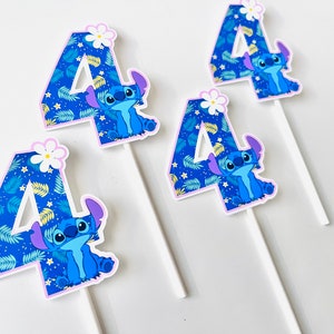 Puede incluir: Cuatro adornos para tartas con el personaje Stitch de Lilo & Stitch. Cada n&uacute;mero cuatro est&aacute; decorado con un patr&oacute;n de hojas tropicales azules y un personaje Stitch. Una flor blanca corona cada n&uacute;mero. Los adornos est&aacute;n sobre palitos blancos.