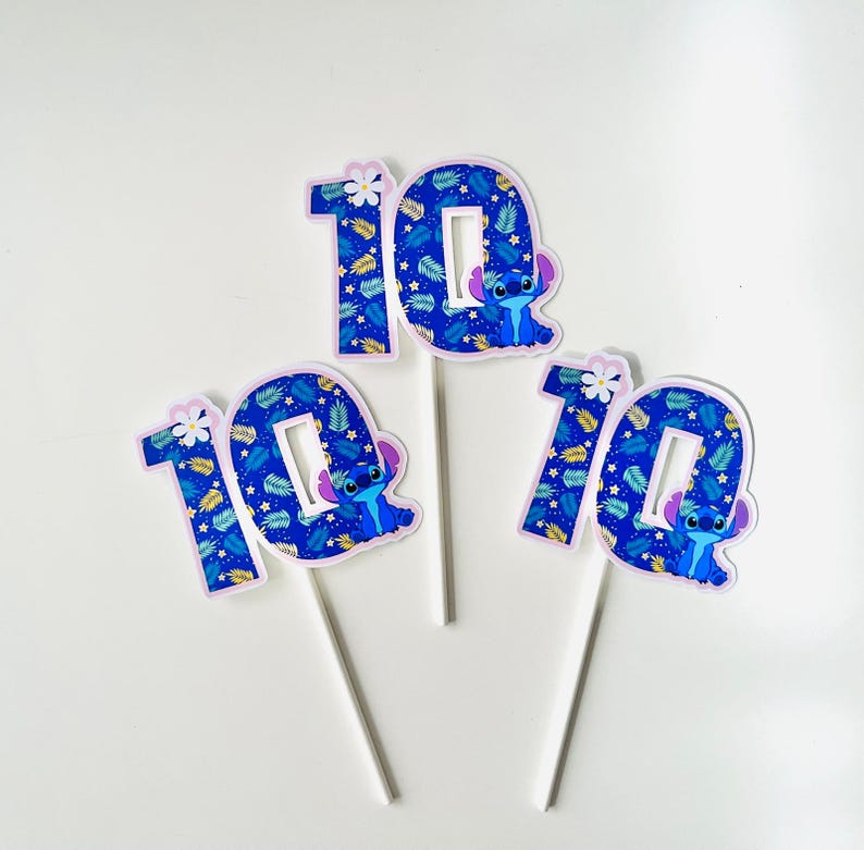 Puede incluir: Tres adornos para tartas con el n&uacute;mero 10, con un personaje de dibujos animados y un estampado de hojas azules. Cada n&uacute;mero est&aacute; sobre un palo blanco. Los adornos son azules, blancos y morados.