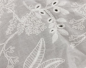 May include: White cotton fabric with delicate white embroidery of floral designs. The embroidery features intricate leaves and flowers.