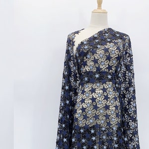 Peut inclure: Tissu en dentelle bleu marine avec un motif d'étoiles. Le tissu est transparent et a une texture délicate.