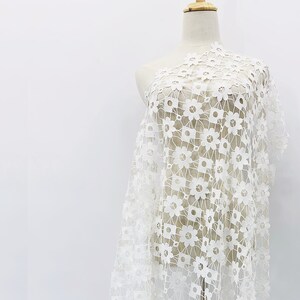May include: White floral lace fabric with a delicate pattern. The lace is lightweight and sheer, making it perfect for a variety of projects.