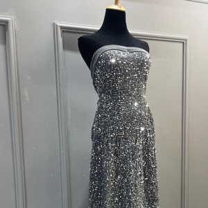 以下が含まれることがあります： ベルベットの裾が付いた、銀色のスパンコールのストラップレスドレスです。