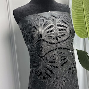May include: Black leather fabric with a delicate floral pattern cut out. The fabric is draped over a black dress form.