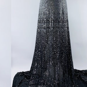 Puede incluir: Una tela de lentejuelas con degradado de plata y negro. La tela está en un maniquí y tiene un acabado liso y brillante.