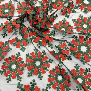 May include: Red and green embroidered hearts on a black mesh fabric. The hearts are arranged in a circular pattern.