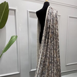 May include: A silver and brown sequined fabric with a leopard print pattern. The fabric is draped over a dress form.