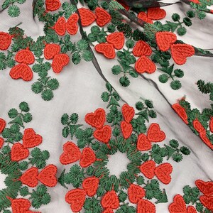 May include: Black mesh fabric with red heart and green leaf embroidery. The fabric has a delicate, lacy texture.