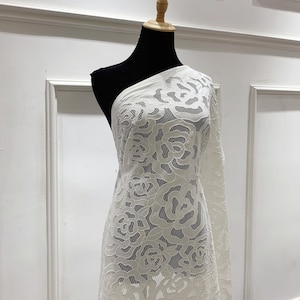 May include: White lace fabric with a floral pattern. The fabric is draped over a white mannequin.