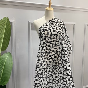 Può includere: Tessuto bianco con un motivo floreale nero. Il tessuto è drappeggiato su un manichino.