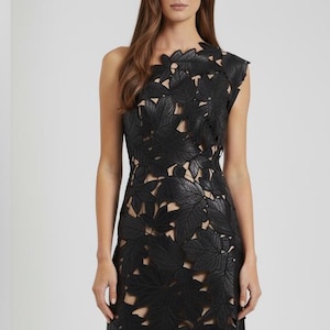 May include: Black, one-shoulder, floor-length dress with a leaf-cutout design. The dress features a fitted bodice and a flowing skirt, and is paired with black ankle boots. The dress is made of a dark material and is suitable for formal events.