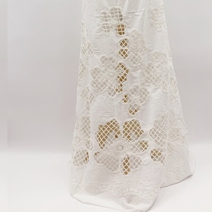 Peut inclure: Tissu en coton blanc avec un d&eacute;licat motif de broderie florale. Le tissu pr&eacute;sente un motif ajour&eacute; et transparent qui cr&eacute;e un aspect d&eacute;licat et a&eacute;rien. Le tissu est parfait pour cr&eacute;er une vari&eacute;t&eacute; de v&ecirc;tements, tels que des robes, des jupes et des chemisiers.