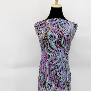 May include: A fabric with a wavy pattern in shades of purple, green, and gold. The fabric is made of sequins and is sheer.