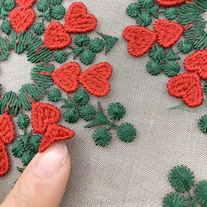May include: Close-up of red embroidered hearts and green leaves on a beige fabric. The hearts are stitched in a simple, classic style.