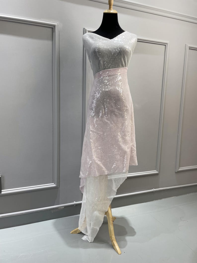 K&ouml;nnte beinhalten: Ein wei&szlig;er und rosa paillettenbesetzter Stoff mit einem High-Low-Saum. Der Stoff ist &uuml;ber eine Schaufensterpuppe drapiert.