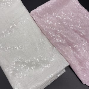 K&ouml;nnte beinhalten: Zwei Stoffst&uuml;cke mit Pailletten. Eines ist wei&szlig; und das andere ist rosa.