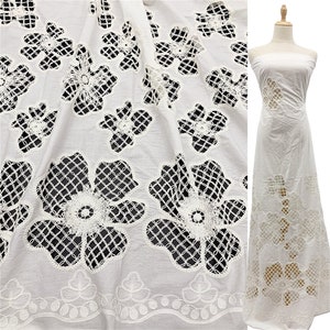 Peut inclure: Tissu en coton blanc avec un motif de dentelle florale d&eacute;licate. Le tissu pr&eacute;sente un motif en forme de grille avec des fleurs d&eacute;coup&eacute;es. Le tissu est pr&eacute;sent&eacute; drap&eacute; sur une surface et &eacute;galement cousu en une longue robe blanche.
