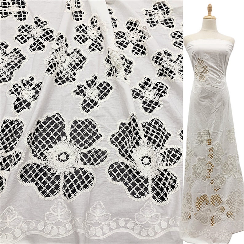 Peut inclure: Tissu en coton blanc avec un motif de dentelle florale d&eacute;licate. Le tissu pr&eacute;sente un motif en forme de grille avec des fleurs d&eacute;coup&eacute;es. Le tissu est pr&eacute;sent&eacute; drap&eacute; sur une surface et &eacute;galement cousu en une longue robe blanche.