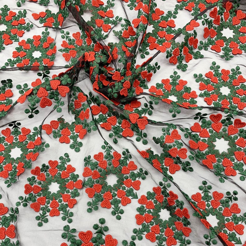 May include: Red and green embroidered hearts on a black mesh fabric. The hearts are arranged in a circular pattern.