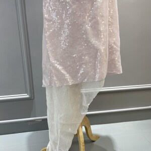 K&ouml;nnte beinhalten: Ein rosa paillettenbesetztes Kleid mit einem wei&szlig;en, durchsichtigen &Uuml;berzug. Das Kleid befindet sich auf einem h&ouml;lzernen Mannequin.