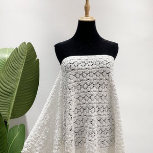 May include: White crochet fabric with a delicate floral pattern. The fabric is draped over a black dress form.