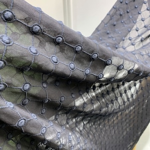Puede incluir: Tela negra transparente con un delicado patr&oacute;n bordado de peque&ntilde;os c&iacute;rculos. La tela es suave y ligera, lo que la hace ideal para ropa o decoraci&oacute;n del hogar.