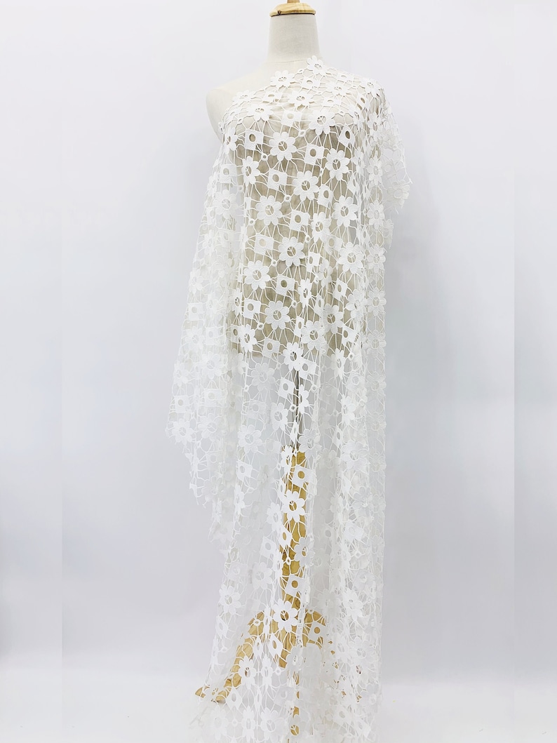 May include: White floral lace fabric with a delicate pattern. The lace is lightweight and sheer, making it perfect for a variety of projects.