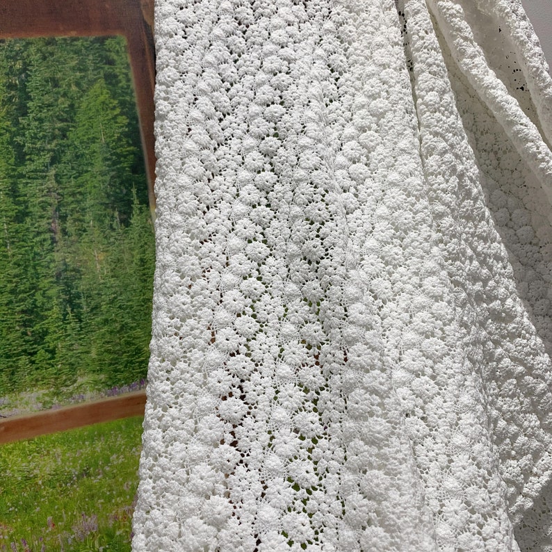 May include: White crochet fabric with a delicate floral pattern. The fabric is soft and airy, making it perfect for a variety of crafting projects.