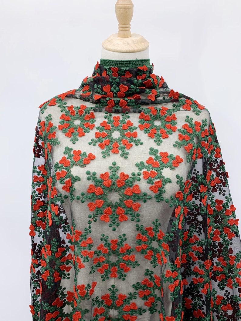 May include: Red and green floral embroidered mesh fabric. The fabric has a repeating pattern of red hearts and green leaves.