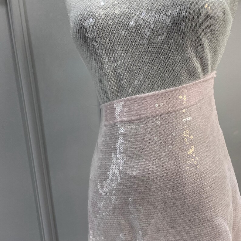 K&ouml;nnte beinhalten: Ein wei&szlig;er Paillettenrock mit einem durchsichtigen &Uuml;berzug. Der Rock ist aus einem weichen, leichten Stoff und hat einen zarten, femininen Look.