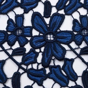 May include: A navy blue lace fabric featuring a repeating floral pattern with embroidered petals and leaves. The design consists of interconnected dark blue threadwork forming openwork shapes between the solid stitched flower motifs.