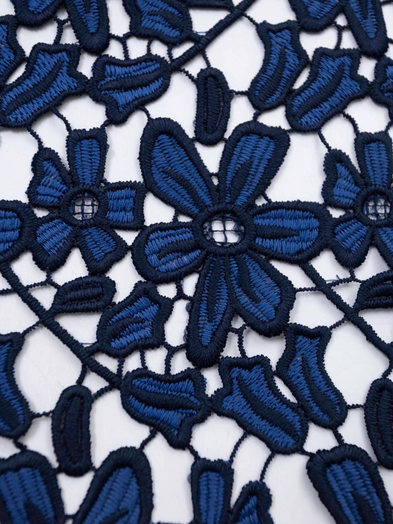 May include: A navy blue lace fabric featuring a repeating floral pattern with embroidered petals and leaves. The design consists of interconnected dark blue threadwork forming openwork shapes between the solid stitched flower motifs.