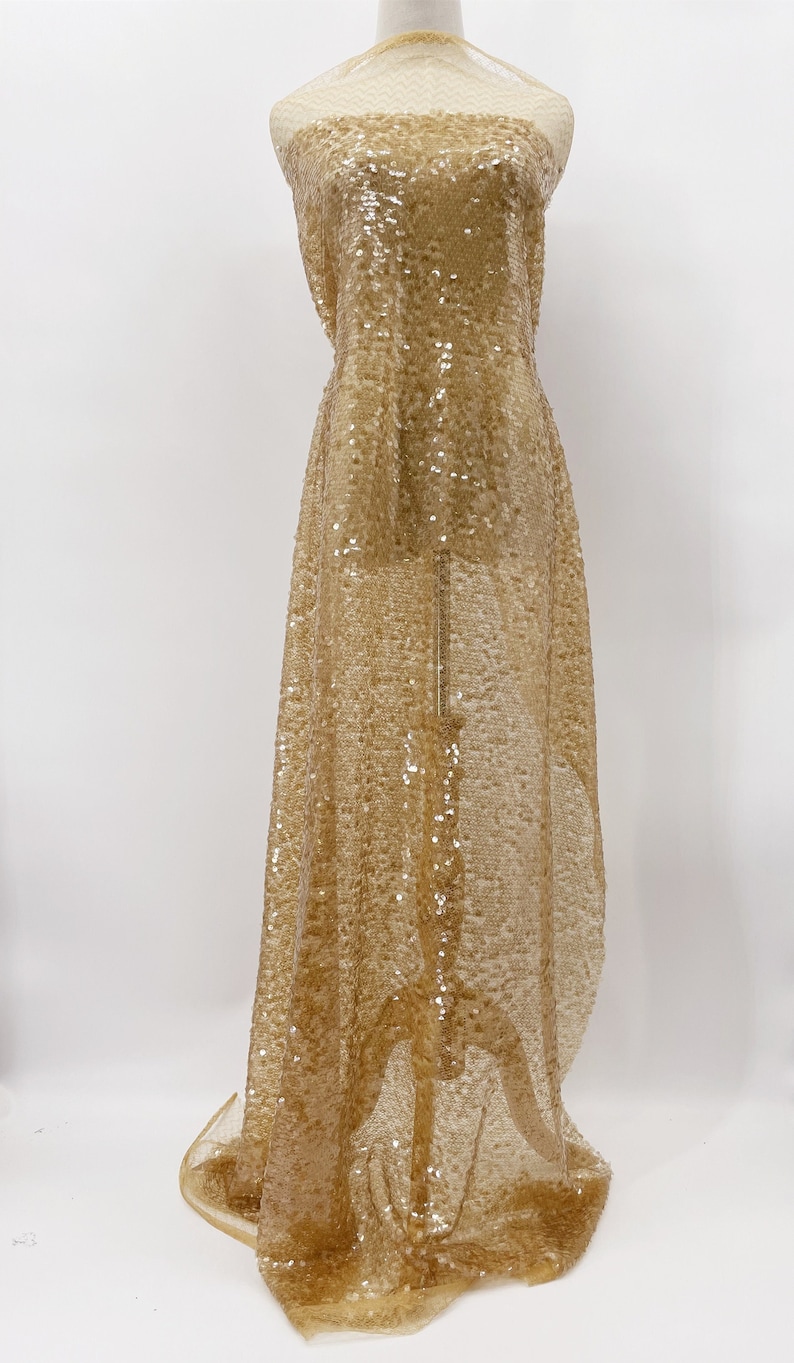 May include: Gold sequined fabric with a sheer mesh backing. The fabric is draped over a dress form.