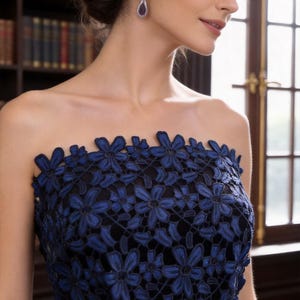 May include: A strapless dress featuring a black base layer overlaid with intricate dark blue floral lace embroidery. The lace pattern consists of repeating flower motifs covering the bodice, accented with small white pearls at the waistline.