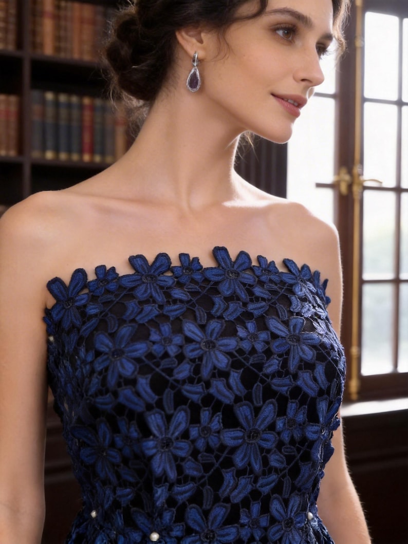May include: A strapless dress featuring a black base layer overlaid with intricate dark blue floral lace embroidery. The lace pattern consists of repeating flower motifs covering the bodice, accented with small white pearls at the waistline.