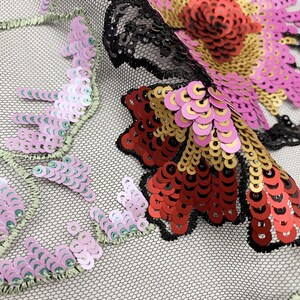 Puede incluir: Primer plano de una tela de malla negra con lentejuelas de colores en forma de flores. Las lentejuelas son en tonos de rosa, rojo, dorado y verde.