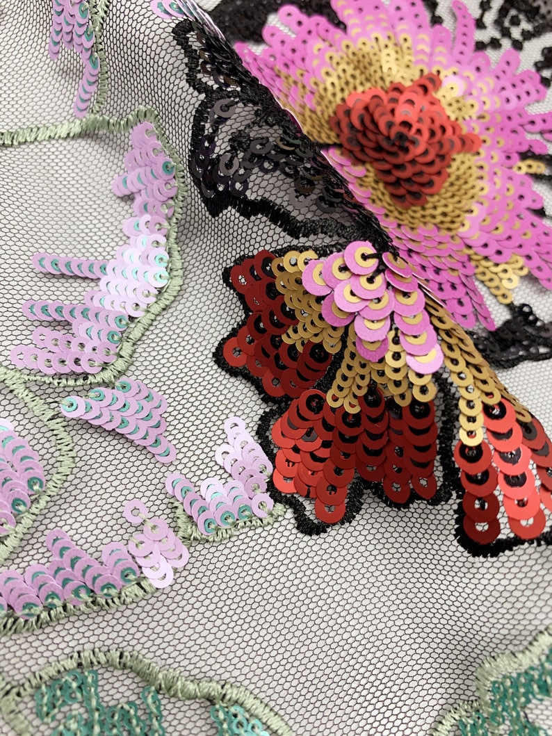 Puede incluir: Primer plano de una tela de malla negra con lentejuelas de colores en forma de flores. Las lentejuelas son en tonos de rosa, rojo, dorado y verde.